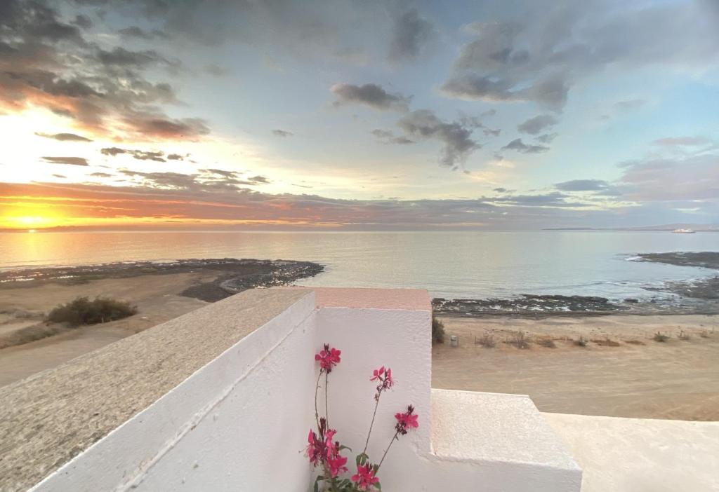a sunset over the ocean with a white wall with flowers at Appartamento Sinestesia Oceanica in Puerto del Rosario