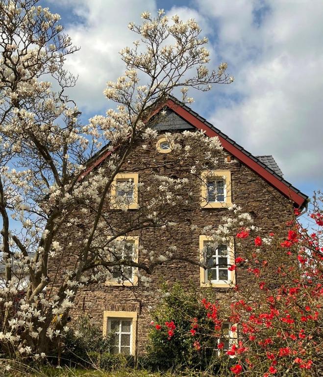 an old stone house with red flowers in front of it at Neu!!! Moselbleibe Altes Forsthaus in Bernkastel-Kues