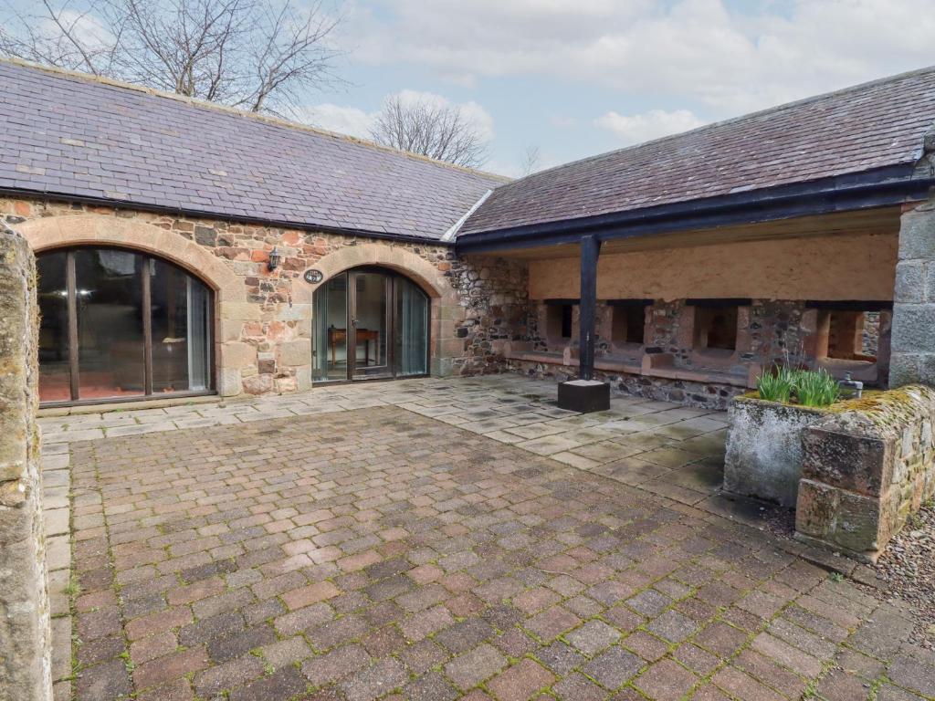 ein altes Backsteingebäude mit einer Terrasse davor in der Unterkunft Fern Cottage in Wooler