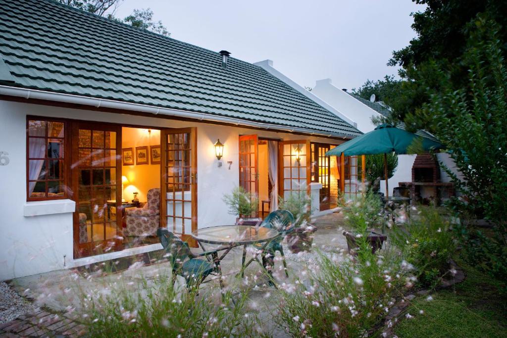 a house with a table and chairs and an umbrella at Swallows Nest Country Cottages in Stormsrivier