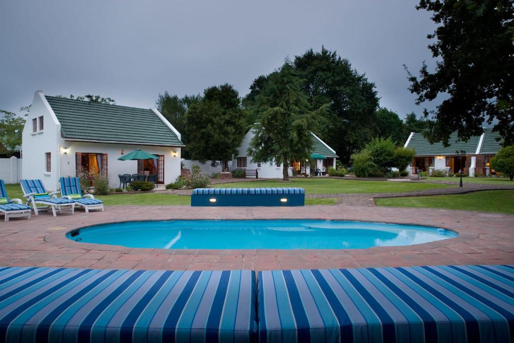 a swimming pool with blue chairs and a house at Swallows Nest Country Cottages in Stormsrivier