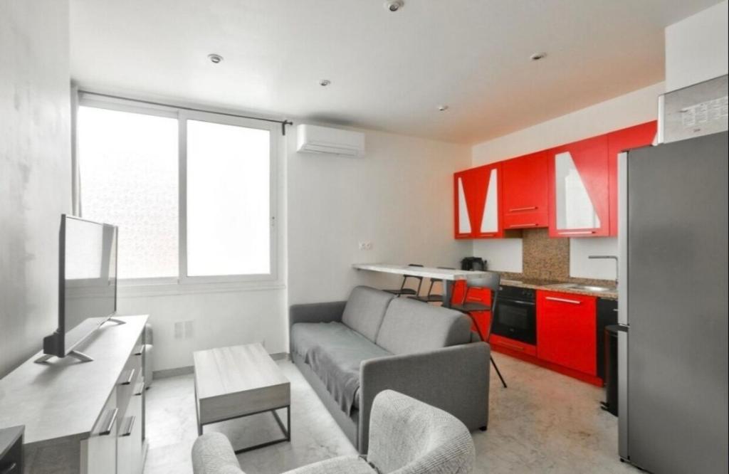 un salon avec un canapé et une cuisine avec des armoires rouges dans l'établissement Nice Libération beautiful 3 rooms- AC Wifi, à Nice