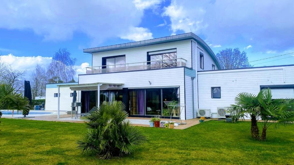a white house with palm trees in the yard at Maison Mélusine ossature bois forêt de Brocéliande in Néant-sur-Yvel