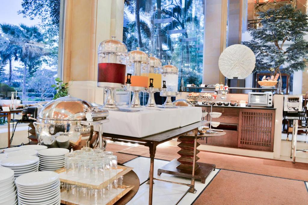 A buffet station with drinks, chafing dishes, plates, and glasses in a bright dining room.