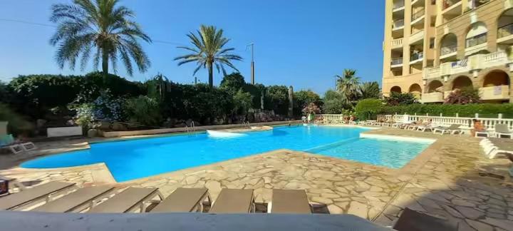 une grande piscine avec des chaises et un bâtiment dans l'établissement Cosy Blue Classé 2 étoiles Piscine Parking Clim Terrasse, à Cannes