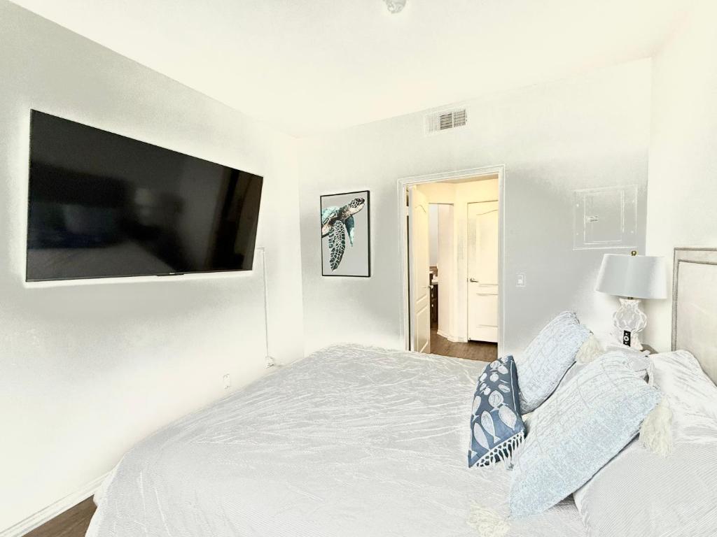 a white bedroom with a bed and a flat screen tv at Spacious and Central with a Pool View in Los Angeles