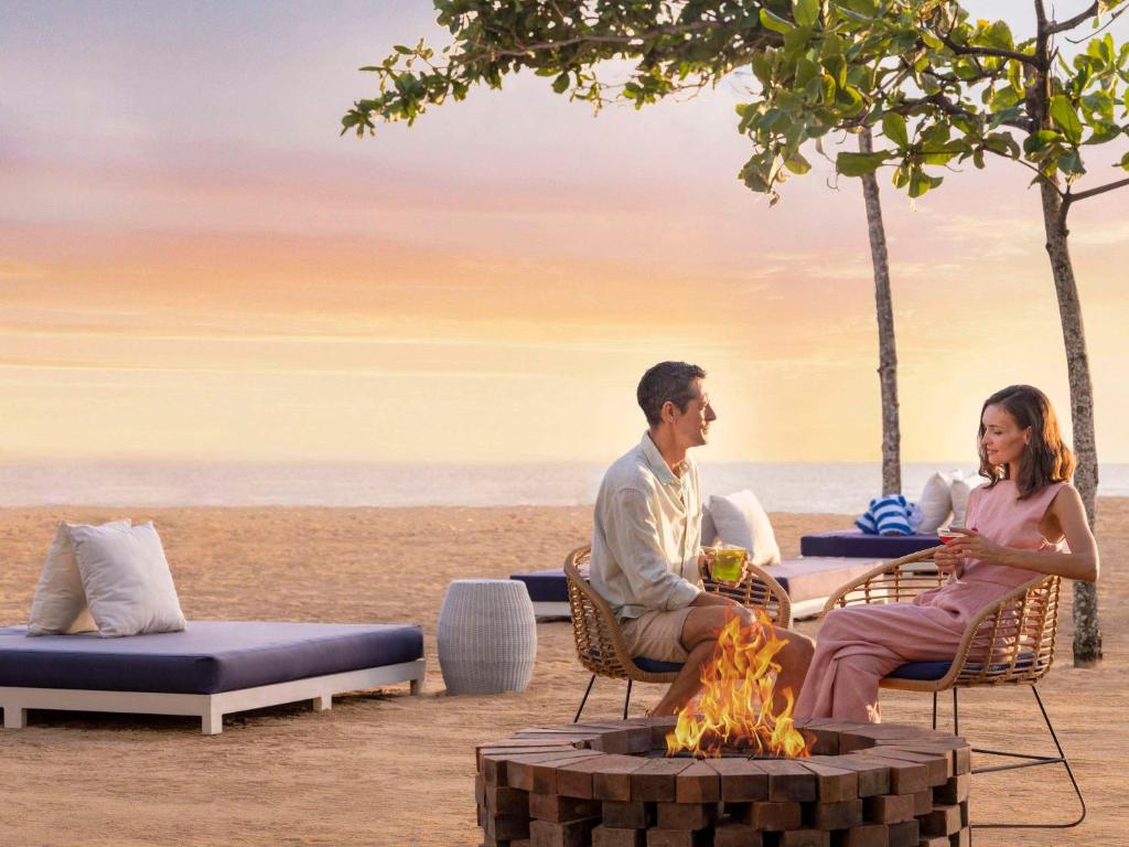 a man and woman sitting around a fire pit on the beach at Sofitel Bali Nusa Dua Beach Resort in Nusa Dua