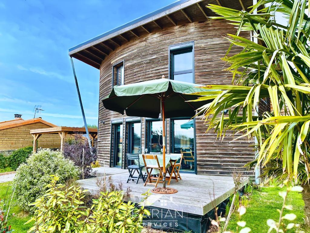 une maison dotée d'une terrasse en bois avec une table et un parasol dans l'établissement Maison en bois 6p à 5km des plages de Fouras, à Saint-Laurent-de-la-Prée