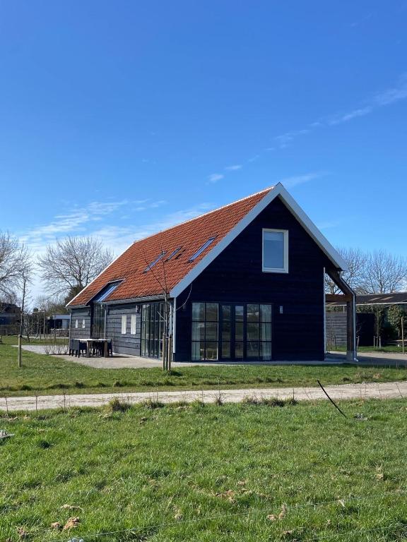 a black house with a red roof on a field at Vrijvakantiehuis Brouwerijweg 45a in Domburg