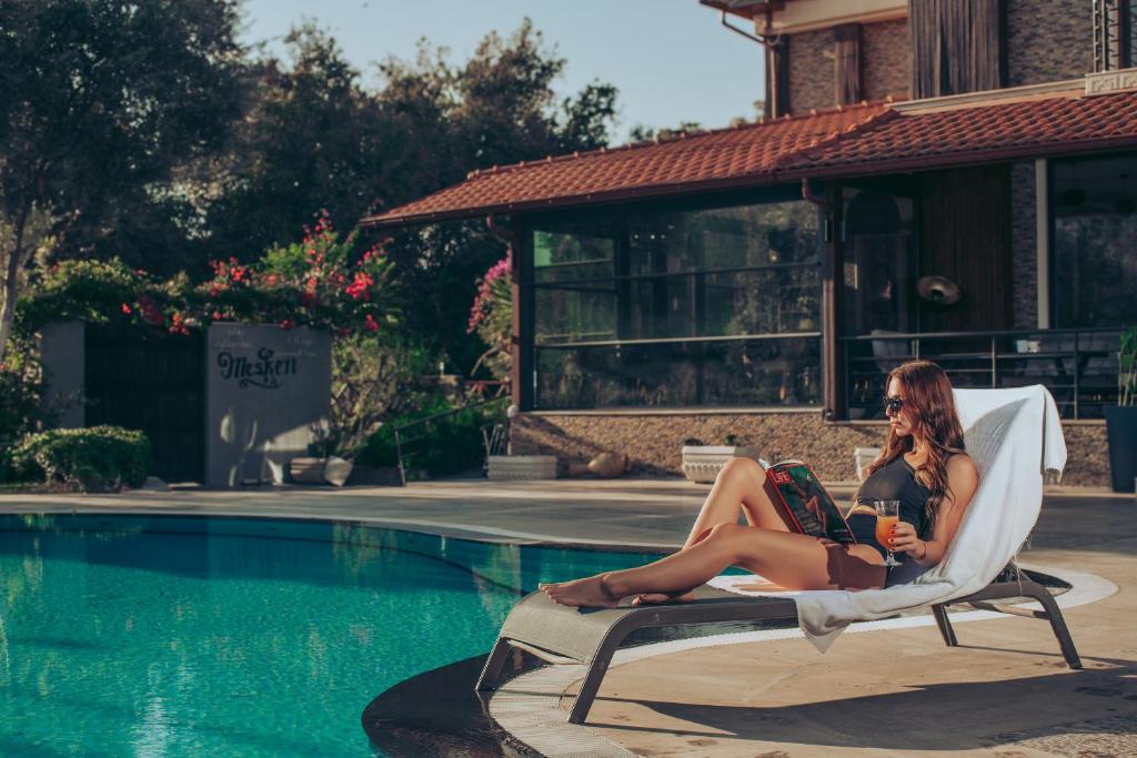 two women sitting on a chair next to a swimming pool at Mesken Inn Göcek Hotel in Göcek
