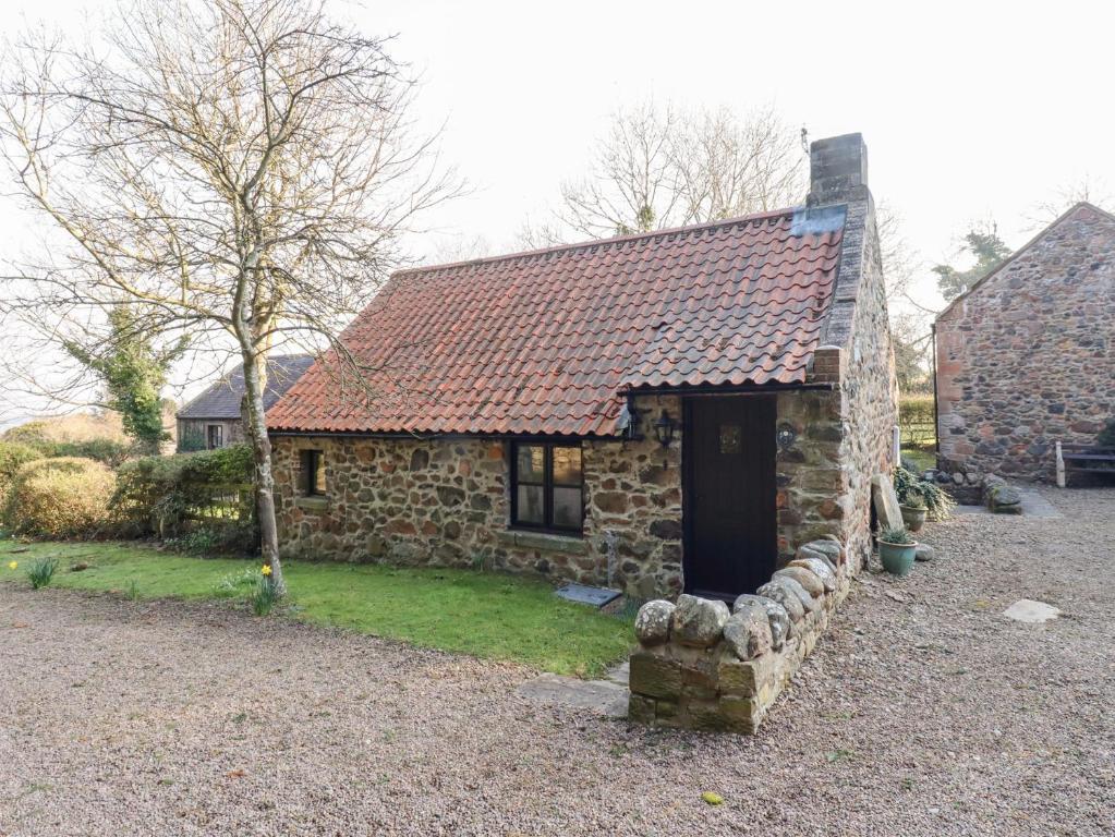 een klein stenen huis met een zwarte deur in een tuin bij Tile Rouge in Wooler