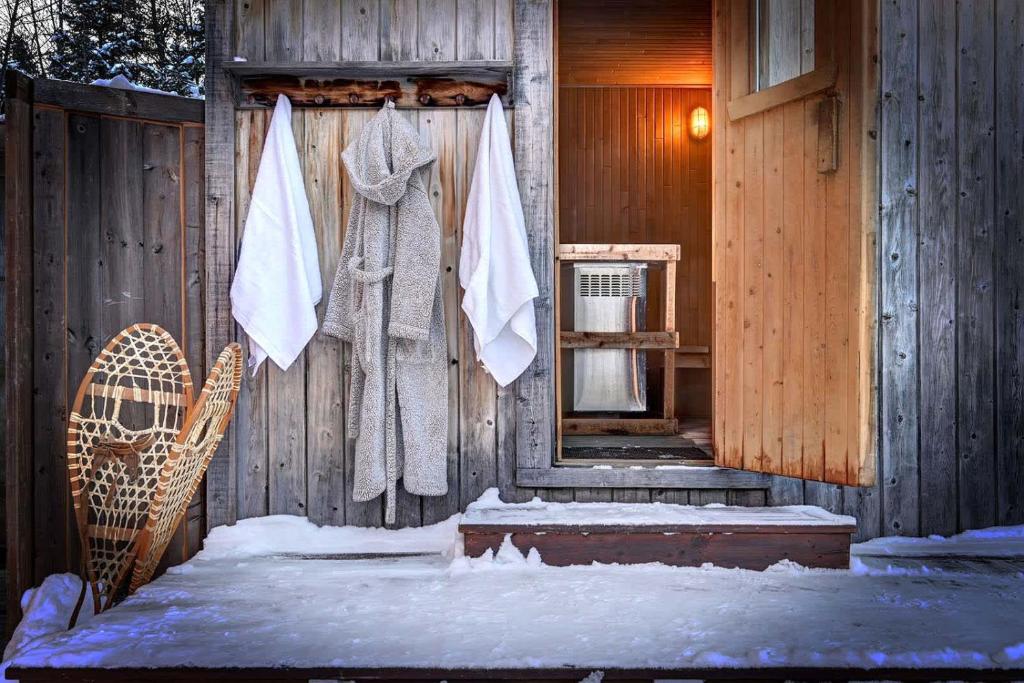 a wooden cabin with snow on the door and towels at Front RIVER private BEACH 2 HOT TUBS 15 p SAUNA in Labelle