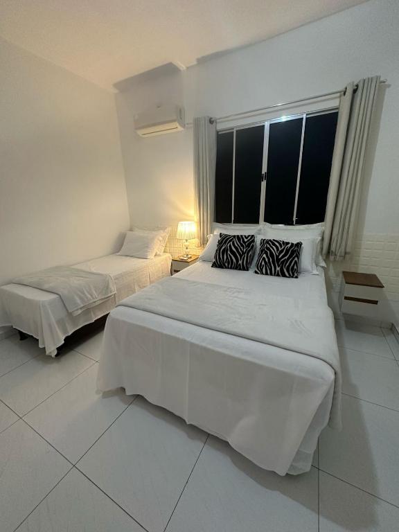 a white bedroom with two beds and a window at Torquato Flats Orla in Petrolina