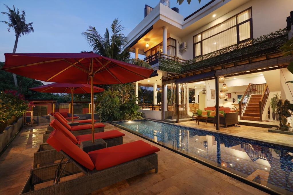 a house with a swimming pool with red chairs and umbrellas at The Magic Villa Keramas in Gianyar