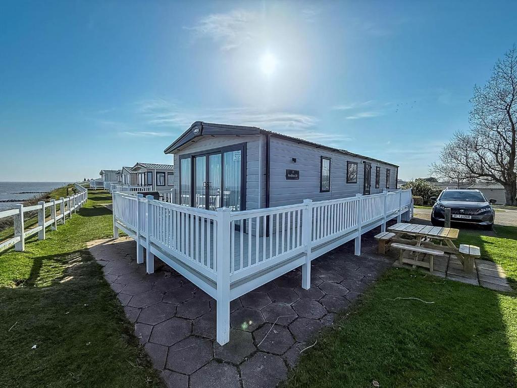 een klein huis met een witte veranda en een geparkeerde auto bij Beautiful Caravan With Stunning Sea Views At Haven Hopton Ref 80001H in Great Yarmouth