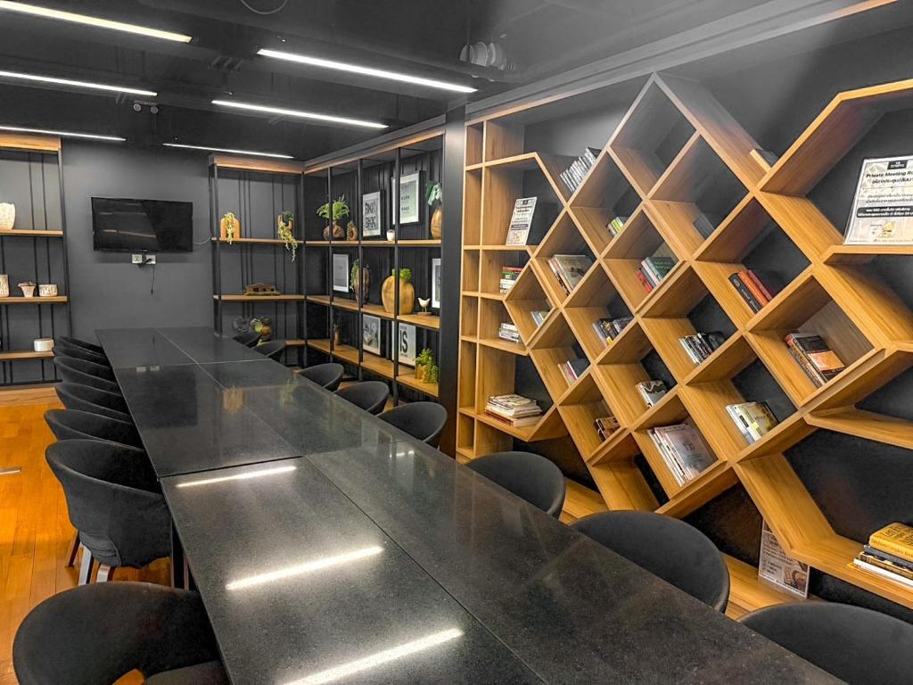 A dark conference table sits beside built-in bookshelves and a wall-mounted screen.