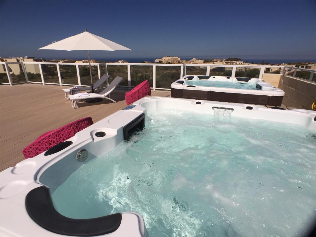 a hot tub on a deck with an umbrella at GozoWindmill Apartments in Qala