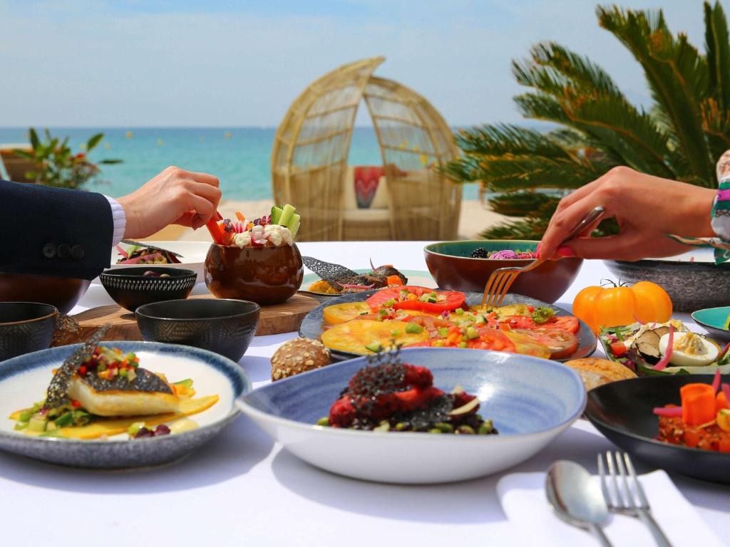 a table with plates of food on the beach at Croisette Beach Hotel Cannes - MGallery Collection in Cannes