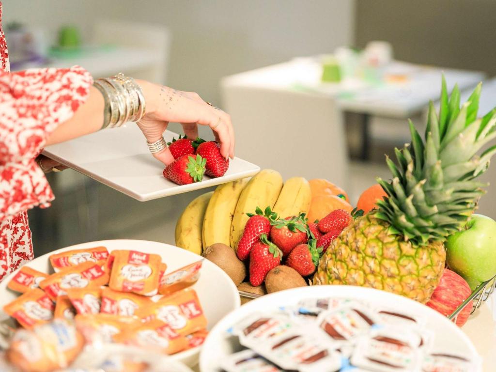 a woman is reaching for a plate of fruit at Ibis Styles Menton Centre in Menton