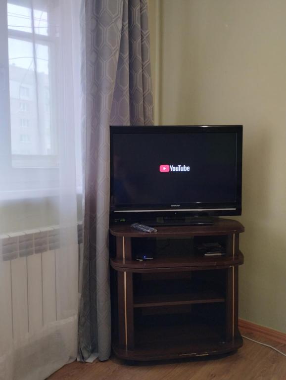 a flat screen tv sitting on a wooden stand next to a window at Уютная квартира рядом с метpo Холодная гора in Kharkiv