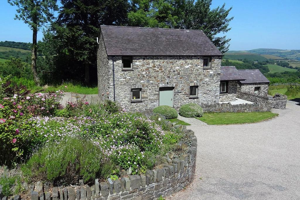 een stenen huis met een stenen muur en bloemen bij Granary Cottage with hot tub on organic farmland in Lampeter