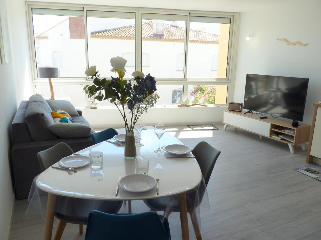 un salon avec une table avec un vase de fleurs dans l'établissement Sol-y-Days Murènes, Appartement moderne rive droite proche plages et centre, au Grau-du-Roi