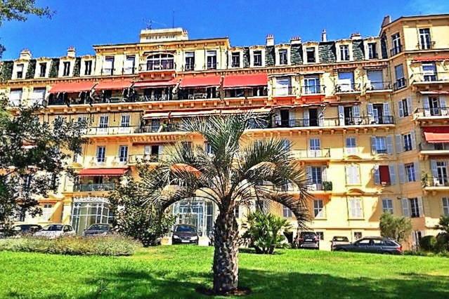 un grand bâtiment avec un palmier devant dans l'établissement Le Palais Bellevue - Cannes, à Cannes