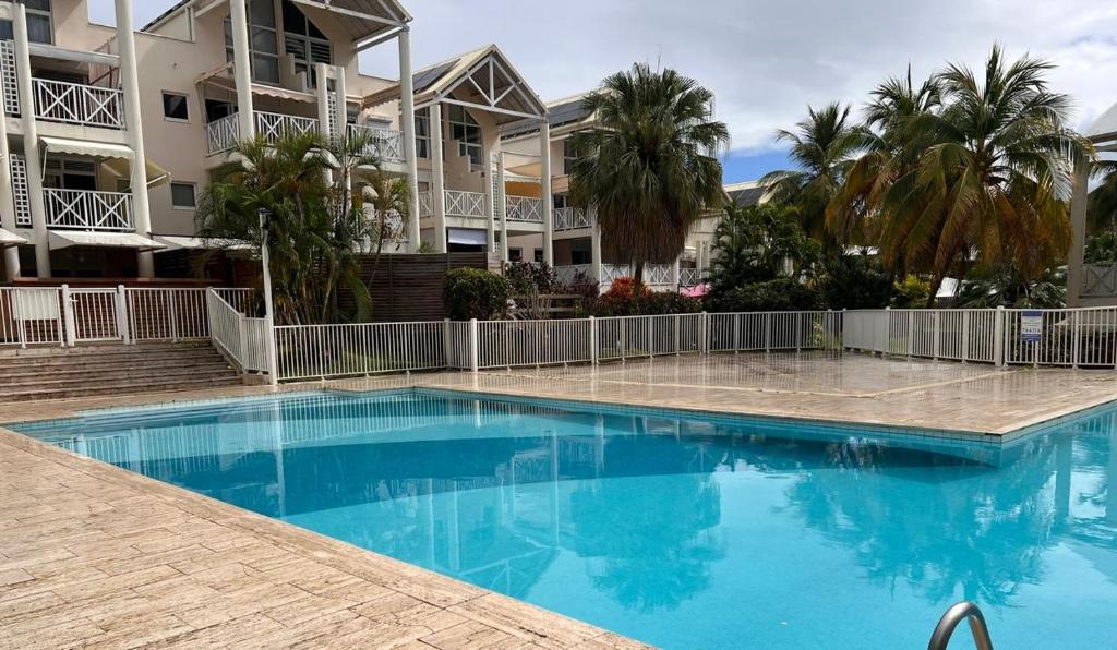 a swimming pool in front of a building with palm trees at Spacieux appartement avec terrasse et piscine au Diamant in Le Diamant
