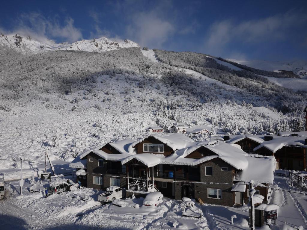 un edificio cubierto de nieve frente a una montaña en Ski Sur Apartments en San Carlos de Bariloche