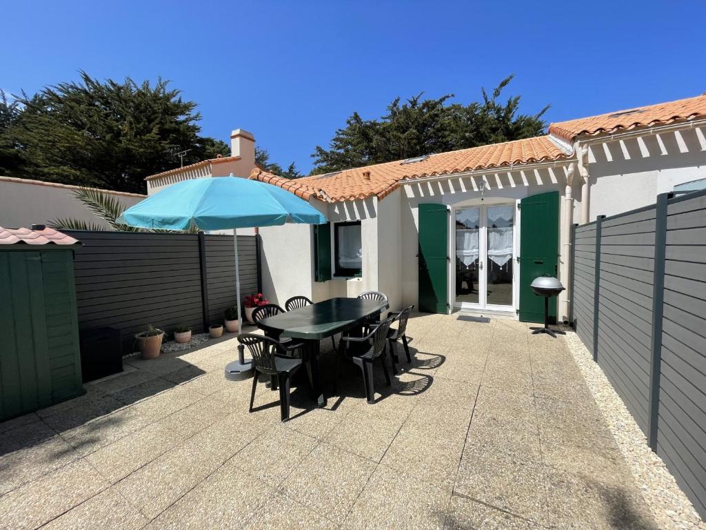 un patio avec une table, des chaises et un parasol dans l'établissement Maisonnette cosy à Barbâtre, bordure forêt, proche plage - FR-1-823-6, à Barbâtre