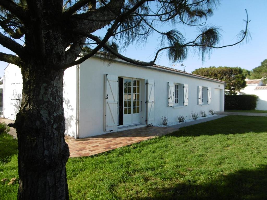 une maison blanche avec un arbre devant dans l'établissement Maison de plain-pied avec jardin ombragé et animaux admis, proche mer et forêt - 6 pers - FR-1-823-30, à La Guérinière