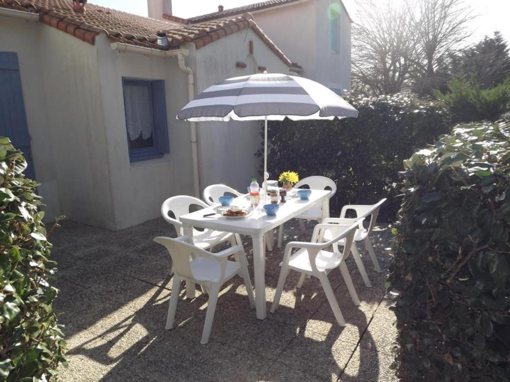 une table blanche avec des chaises et un parasol dans l'établissement Maison mitoyenne confortable, proche plage et forêt - FR-1-823-35, à Barbâtre