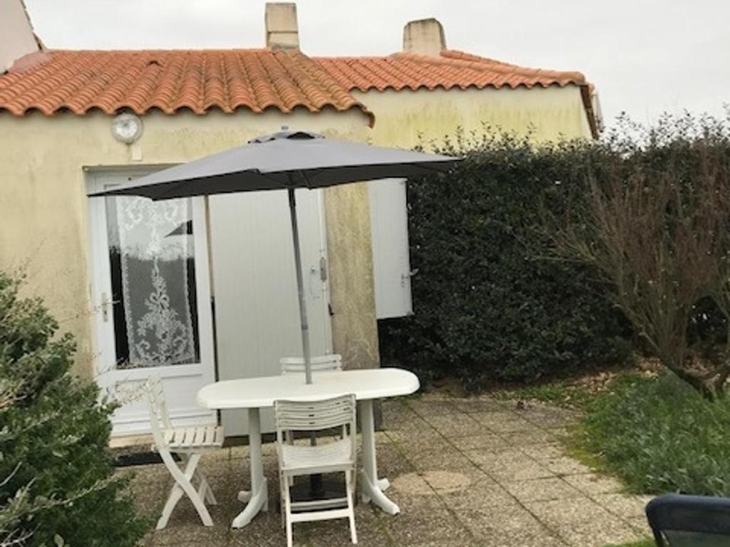 - une table et des chaises avec un parasol en face d'une maison dans l'établissement Maisonnette à 30m de la plage pour 4 pers - Barbâtre - FR-1-823-96, à Barbâtre