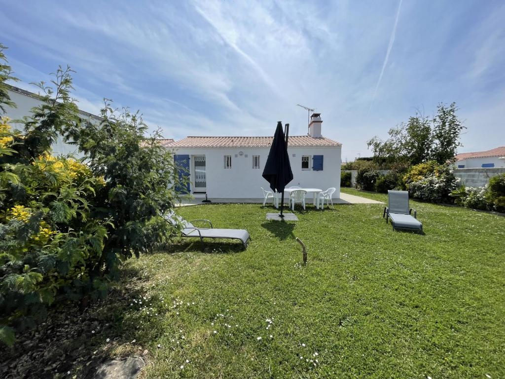 une cour avec des chaises et un parasol ainsi qu'une maison dans l'établissement Maison calme Noirmoutier Plage Sableaux, Animaux admis - FR-1-823-134, à Noirmoutier-en-l'lle