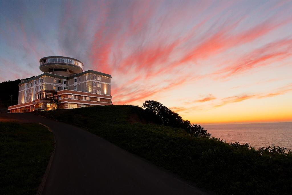 a building on a hill next to the ocean at sunset at Hotel Neu Schloss Otaru in Otaru