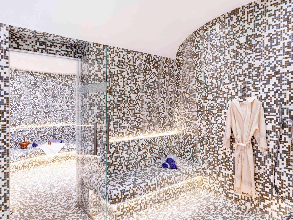 a tiled bathroom with a robe hanging on a wall at Pullman Doha West Bay in Doha
