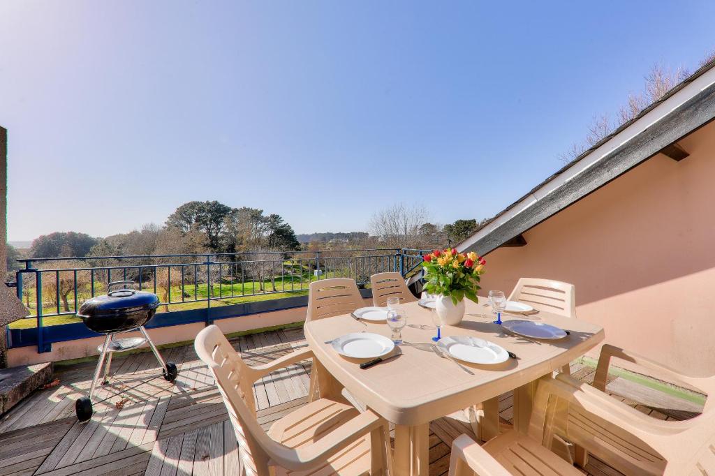 une terrasse en bois avec une table et des chaises sur un balcon dans l'établissement Appartement avec terrasse vue mer pour 6 - Arzon, à Arzon