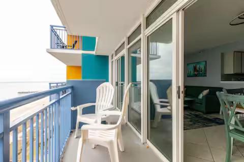einen Balkon mit zwei weißen Stühlen und ein Wohnzimmer in der Unterkunft Oceanfront Luxury 2BR King Suite Atlantica Resort in Myrtle Beach