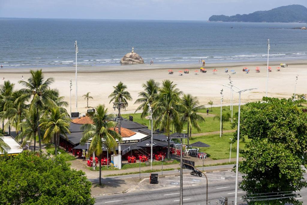 Una playa con un edificio y palmeras y el océano. en Otimo apartamento a 200m do mar com WiFi, en Campo Grande