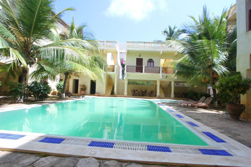 a swimming pool in front of a house with palm trees at Jannataan Hotel in Lamu