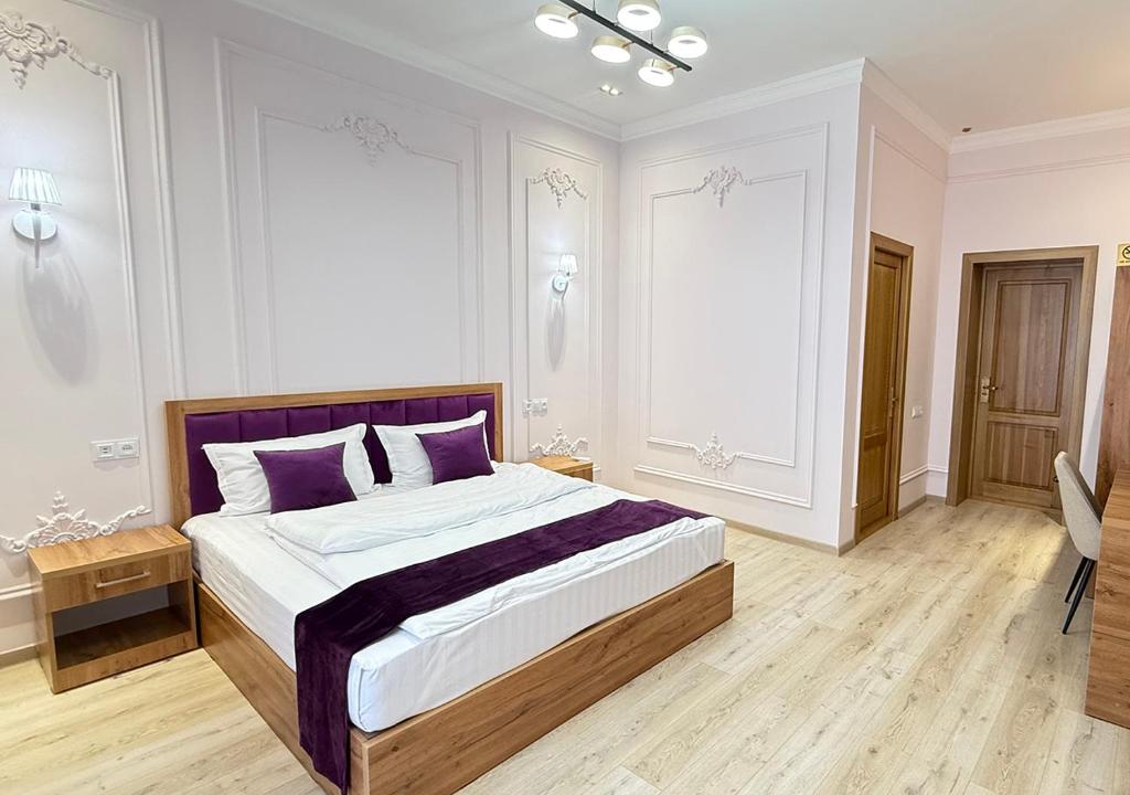 ein weißes Schlafzimmer mit einem großen Bett mit lila Kissen in der Unterkunft Mumtoz East Hotel in Buxoro