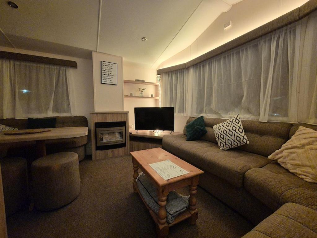 ein Wohnzimmer mit Sofa und Tisch in der Unterkunft Cosy Perranporth caravan, Cornwall in Perranzabuloe
