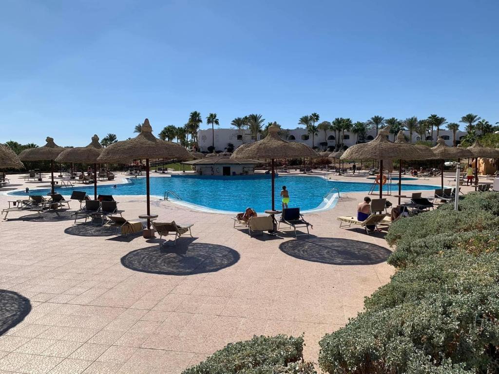 a pool with chairs and umbrellas and people sitting around it at Domina Coral Bay Sultan Vista Mare Uno in Banī Ghālib