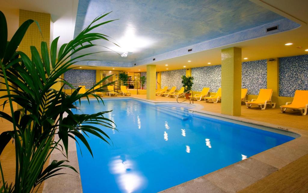 a large swimming pool in a hotel with yellow chairs at Playas de Liencres - Hotel & Apartamentos in Boó de Piélagos