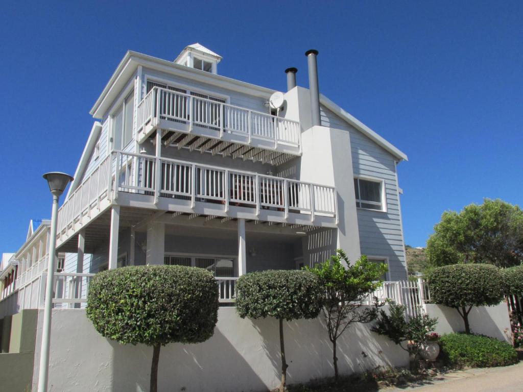 a white house with a balcony and bushes at Point Village Accommodation - Hennie Bottom in Mossel Bay