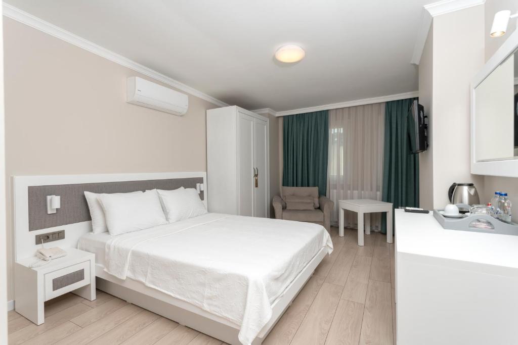 a white bedroom with a bed and a chair at Bay Nihat Otel Lale in Ayvalık