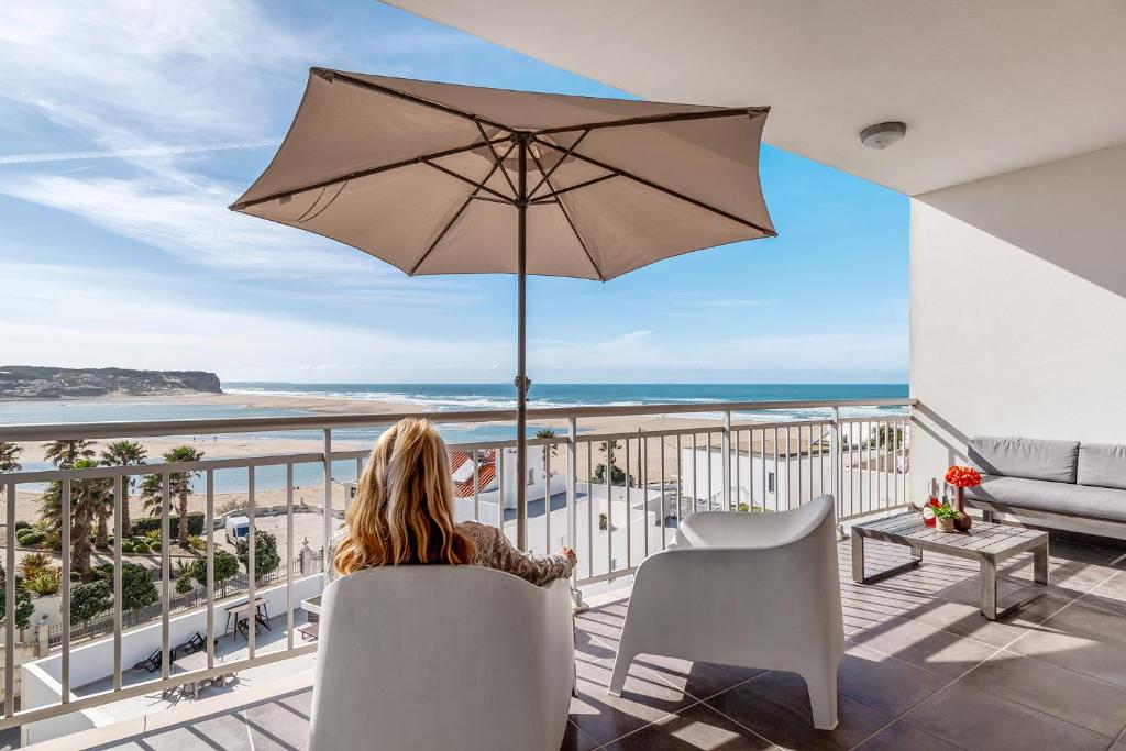 a woman sitting on a balcony with an umbrella at FozPenthouse in Foz do Arelho
