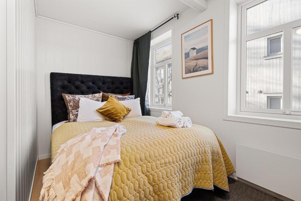 a bedroom with a bed with a yellow comforter and two windows at Nord Apartments in Trondheim