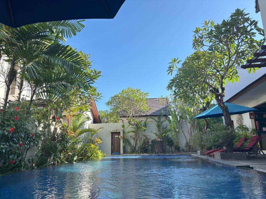a swimming pool in front of a house with trees at The Calna Villa Bali in Kuta
