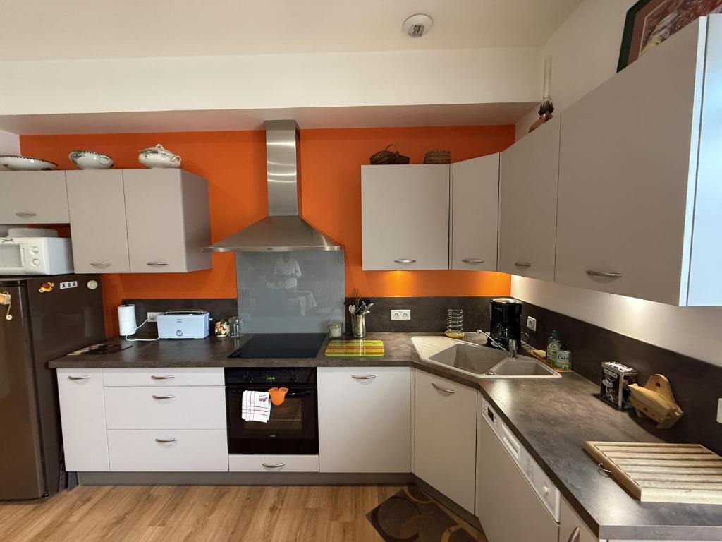 - une cuisine avec des placards blancs et un mur orange dans l'établissement Le Chanzy - Centre - 7 pers - Reve au Mans, au Mans